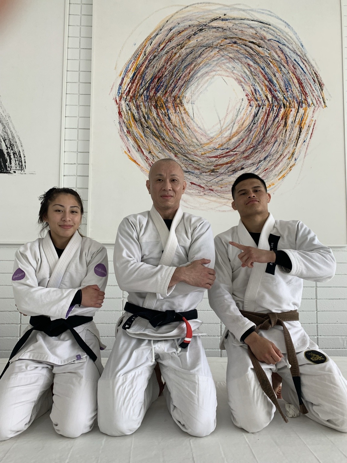 Three jiu-jitsu practitioners in white gis kneeling together on the mat