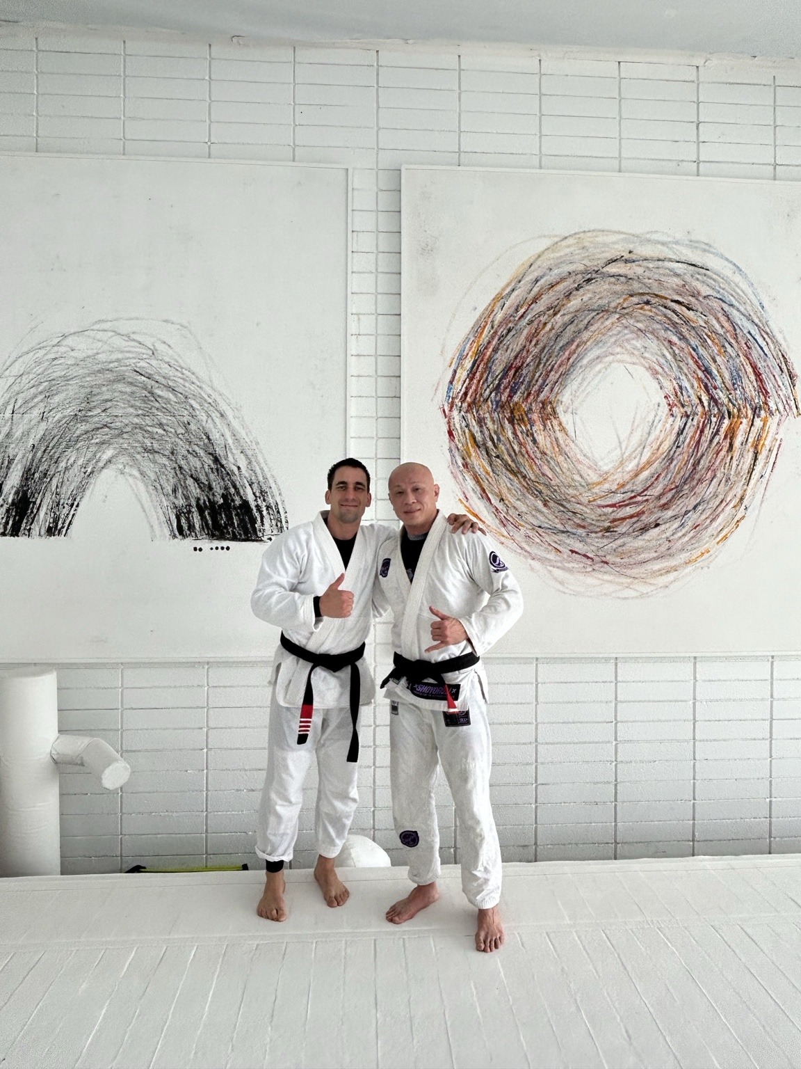 Two jiu-jitsu black belts in white gis standing together on the mat