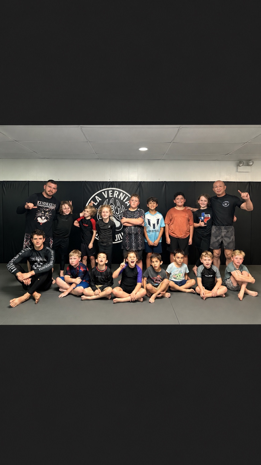 Young students and two adults gathered for a group photo on the academy mat