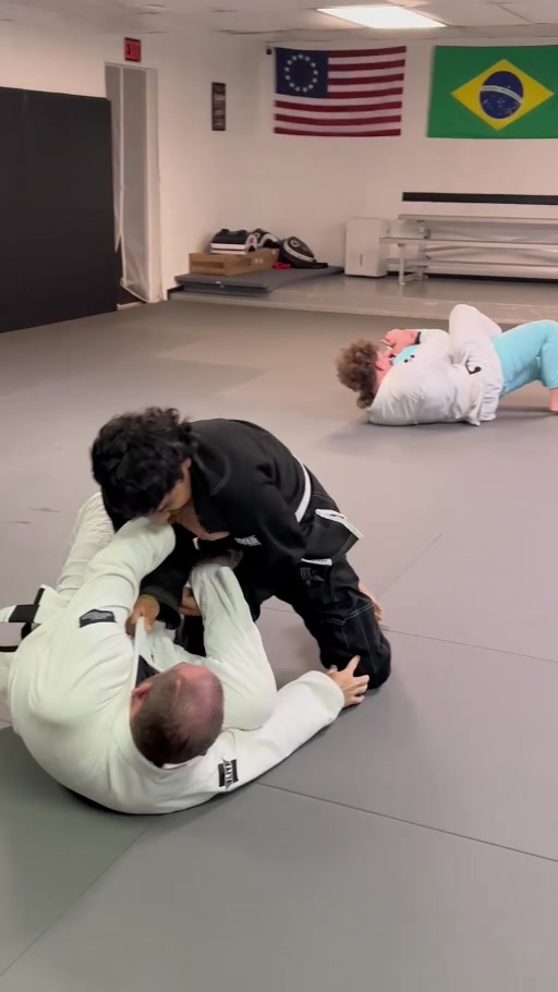Two training partners working grips on the mat, with another pair practicing behind them